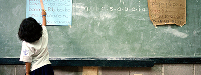 A girl is writing on a blackboard in a primary school to represent the social pillar.